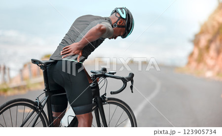 Fitness, sports injury and back pain by man cyclist feel uncomfortable while cycling along mountain route. Training, pain and injured athletic guy suffering from joint, muscle and spinal discomfort 123905734