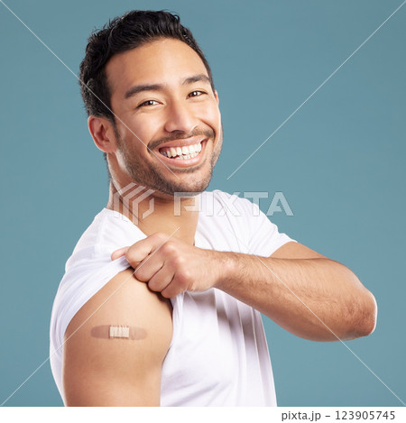 Studio, happy man and portrait with plaster for vaccine, injection wound and safety for Influenza. Blue background, male person and smile with bandage for healthcare, medicine and treatment for virus 123905745