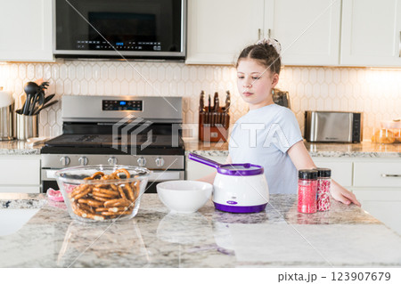 With focused attention, this budding culinary artist dips pretzels into a pot of melted chocolate, creating sweet delights in the warmth of a well-lit home kitchen. 123907679