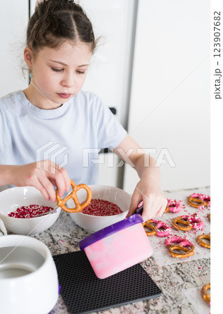 With focused attention, this budding culinary artist dips pretzels into a pot of melted chocolate, creating sweet delights in the warmth of a well-lit home kitchen. 123907682