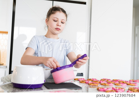 With focused attention, this budding culinary artist dips pretzels into a pot of melted chocolate, creating sweet delights in the warmth of a well-lit home kitchen. 123907684