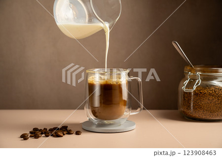 Pouring milk in a glass cup mug of coffee, instant coffee drink 123908463