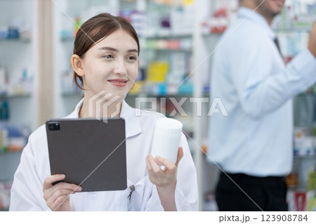 woman pharmacists are selecting medications for patients online via tablet in drug store. Drug seller use tablet holding medicine bottle check for information before sending to patient. 123908784