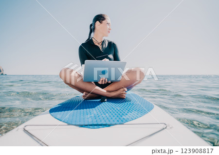 Digital nomad, freelancer, laptop. Happy smiling woman working on sup board at calm sea beach, relieves stress from work. Freelance, remote work on vacation, travel and holidays concept. 123908817