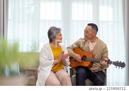 Happy asian senior elderly couple take it easy on retirement holidays playing guitar having fun in living room at home, Happiness singing together. Taking care of each other health in old age. 123909212