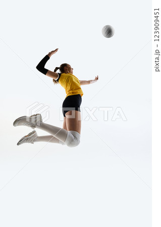Low angle view of young athlete hitting volleyball, showing energy of game, training against white studio background. 123909451