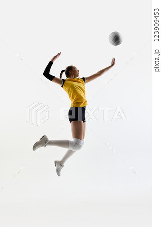 Full-length image of focused young woman, volleyball player in yellow jersey and black short training against white studio background Full-length image of focused young woman, volleyball player in yellow jersey and black short training against white studio background 123909453