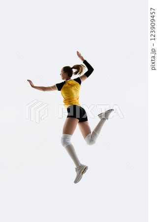 Full-length of young woman, volleyball player n yellow jersey and black shorts jumping, training isolated on white background. 123909457