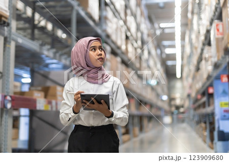 Muslim female wearing hijab warehouse worker holding tablet checks stock on shelf storehouse. businesswoman islamic entrepreneurs rent a warehouse. 123909680