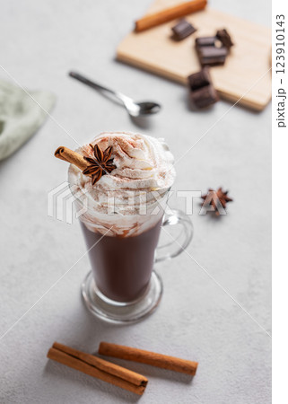 Hot chocolate with whipped cream, cinnamon and spices in a tall glass on a light background Hot chocolate with whipped cream, cinnamon and spices in a tall glass on a light background 123910143