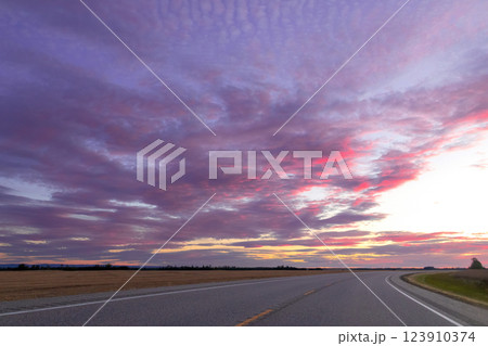 Purple and pink sunset sky with clouds above countryside road. Purple and pink sunset sky with clouds above countryside road. 123910374