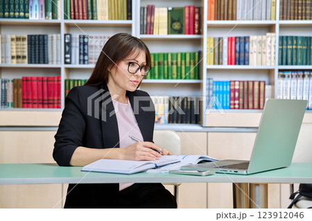 Middle aged female teacher working inside library office with laptop 123912046