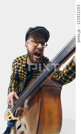 Expressive man, musician unleashing full energy on double bass, wild passion reflected in aggressive playing style. 123912203