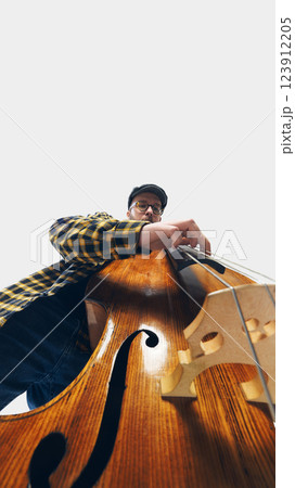 Low-angle image of dedicated bassist immersed in deep, soulful performance, playing double bass against white background. 123912205