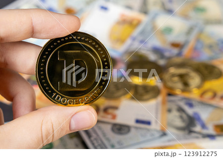 hand holding dogecoin over blurred background of euro and dollar bills, representing cryptocurrency investment and global finance 123912275
