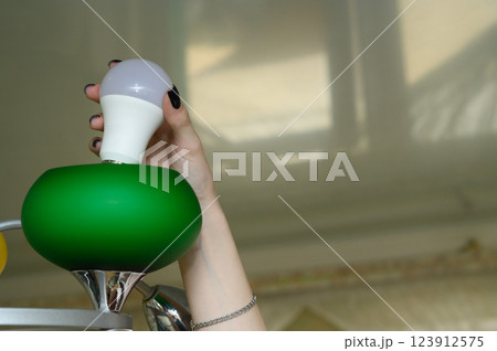 A woman's hand changes an LED light bulb in a lampshade, highlighting the concept of energy efficiency. The image emphasizes modern lighting solutions and the simplicity of DIY home tasks A woman's hand changes an LED light bulb in a lampshade, highlighting the concept of energy efficiency. The image emphasizes modern lighting solutions and the simplicity of DIY home tasks 123912575