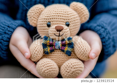 Child holding adorable handmade crochet teddy bear with bow tie 123913514