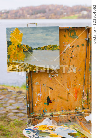 Autumn landscape painting on canvas displayed on an easel by a lake outdoors Autumn landscape painting on canvas displayed on an easel by a lake outdoors 123914062