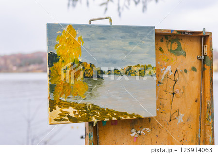 Autumn landscape painting on canvas displayed on an easel by a lake outdoors 123914063