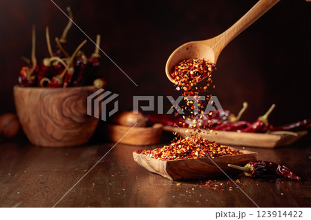 Chilli flakes are poured into a wooden dish. Chilli flakes are poured into a wooden dish. 123914422