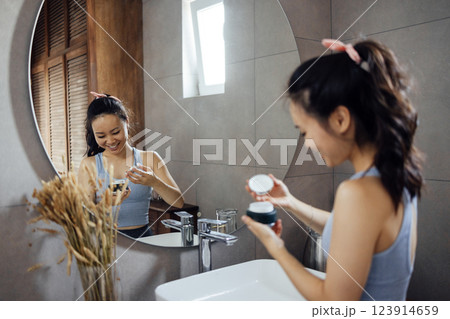 Asian young woman applies moisturizing cream to her face Asian young woman applies moisturizing cream to her face 123914659
