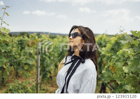 Attractive brunette girl in elegant dress and sunglasses walks through vineyard Attractive brunette girl in elegant dress and sunglasses walks through vineyard 123915120