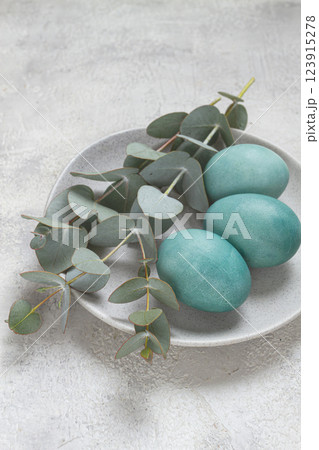 Easter colored eggs, in turquoise tones, on a gray plate, with a branch of eucalyptus, Easter card, top view, no people 123915278