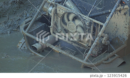 Close-up of a muddy off-road vehicle stuck in deep mud. The radiator fan installed in the rear of the car is rotating. Extreme mud racing Close-up of a muddy off-road vehicle stuck in deep mud. The radiator fan installed in the rear of the car is rotating. Extreme mud racing 123915426