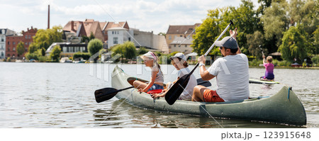Man with two children enjoy having fun paddling canoe rent across lake river water wearing bright orange life vests hot sunny summer day. Healthy recreational activity lifestyle vacation trip journey 123915648