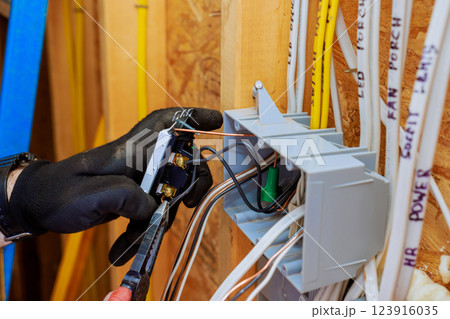 Electrician contractor wearing gloves connects wires to switch light, installation in new home under construction. 123916035