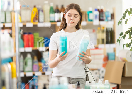 Girl buyer chooses shampoo or shower gel in household goods department of supermarket Girl buyer chooses shampoo or shower gel in household goods department of supermarket 123916594