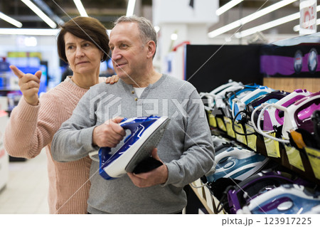 Middle aged wife and husband picking new clothes iron in store Middle aged wife and husband picking new clothes iron in store 123917225