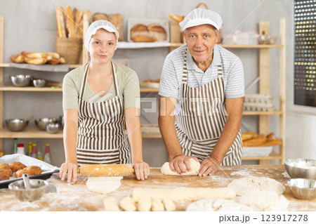 Elderly baker teaching granddaughter to knead and roll dough Elderly baker teaching granddaughter to knead and roll dough 123917278