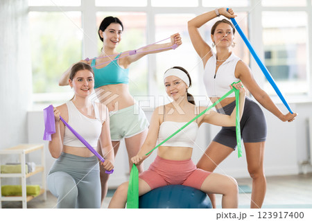 Portrait of sporty girls in sportswear with fitness balls and resistance bands posing together in sports studio, ready for training Portrait of sporty girls in sportswear with fitness balls and resistance bands posing together in sports studio, ready for training 123917400