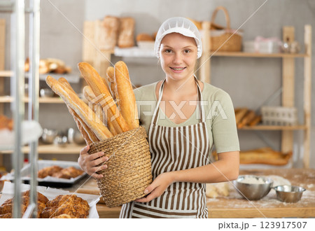Young female baker with basket of baguettes Young female baker with basket of baguettes 123917507
