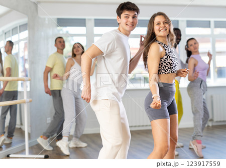 Happy young woman and man with group of international dancers training twist or rock and roll dance in dance class Happy young woman and man with group of international dancers training twist or rock and roll dance in dance class 123917559