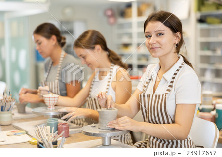 Three craftsperson are busy sculpting from clay and painting ceramic products Three craftsperson are busy sculpting from clay and painting ceramic products 123917657