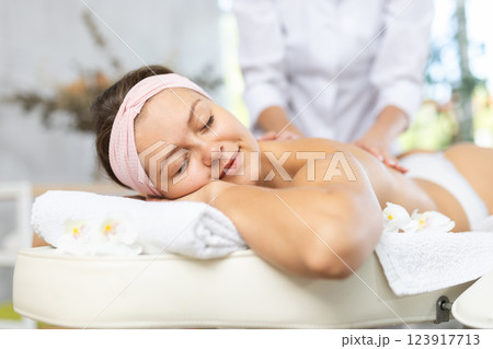Young woman enjoying back and shoulders massage from professional masseuse 123917713