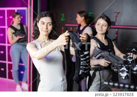 Girls try on a matching vest for playing laser tag in dark room Girls try on a matching vest for playing laser tag in dark room 123917828