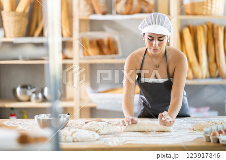 Young female baker kneading dough on table 123917846