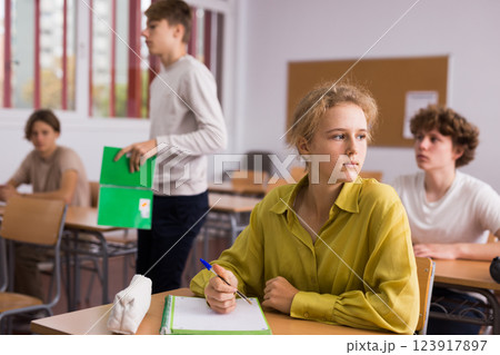 Teenage students studying in classroom with teacher, writing lectures in workbooks 123917897