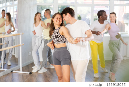Happy young man and girl with group of international dancers training active swing in dance class Happy young man and girl with group of international dancers training active swing in dance class 123918055