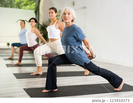 Woman with group of adult people doing stretching workout for body flexibility in yoga studio 123918373