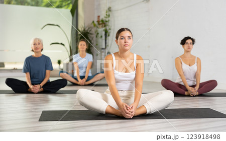 Concentrated young woman performing Butterfly Pose Baddha Konasana during yoga class with female group Concentrated young woman performing Butterfly Pose Baddha Konasana during yoga class with female group 123918498