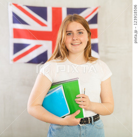 Female student with notebooks stands against wall under flag of Great Britain. Gray background 123918506