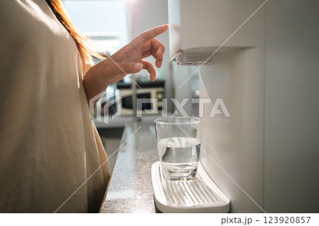 Close up of a woman hand pressing button on a sleek water purifier to dispense fresh, clean water into a glass Close up of a woman hand pressing button on a sleek water purifier to dispense fresh, clean water into a glass 123920857