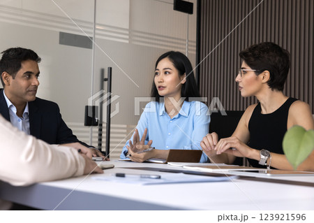 Diverse business partners listen to young Asian woman at table Diverse business partners listen to young Asian woman at table 123921596