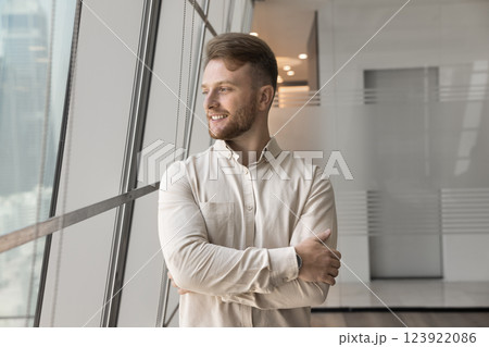 Cheerful millennial businessman look on cityscape in office window 123922086