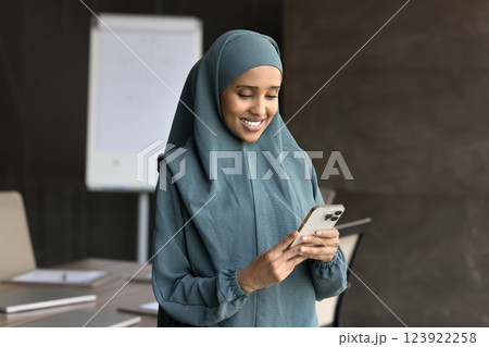 Smiling Arabian businesswoman holds smartphone standing in office 123922258