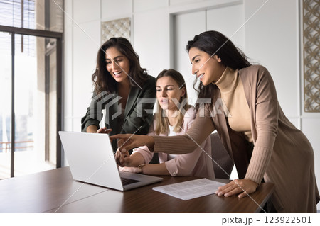 Three multiethnic women colleagues using laptop collaborate on joint task 123922501